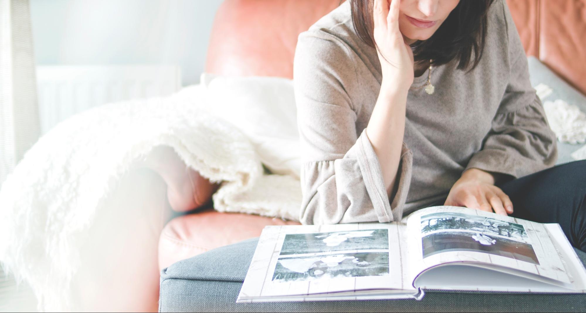 A woman sitting on a couch reading a wedding photo book.