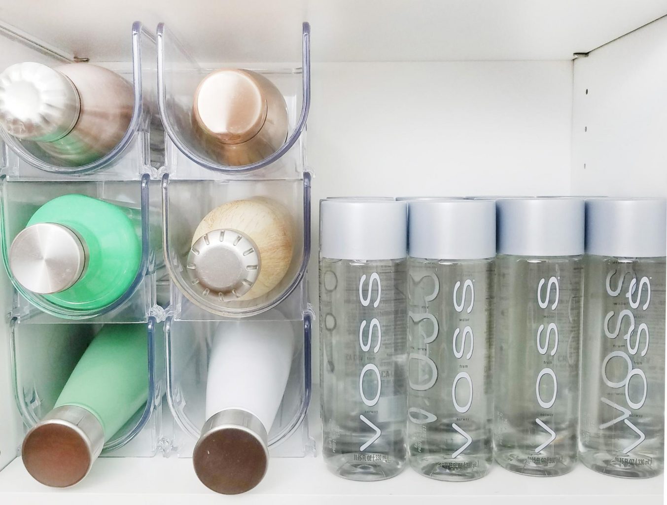 A bathroom with organized bottles of water in a cabinet.