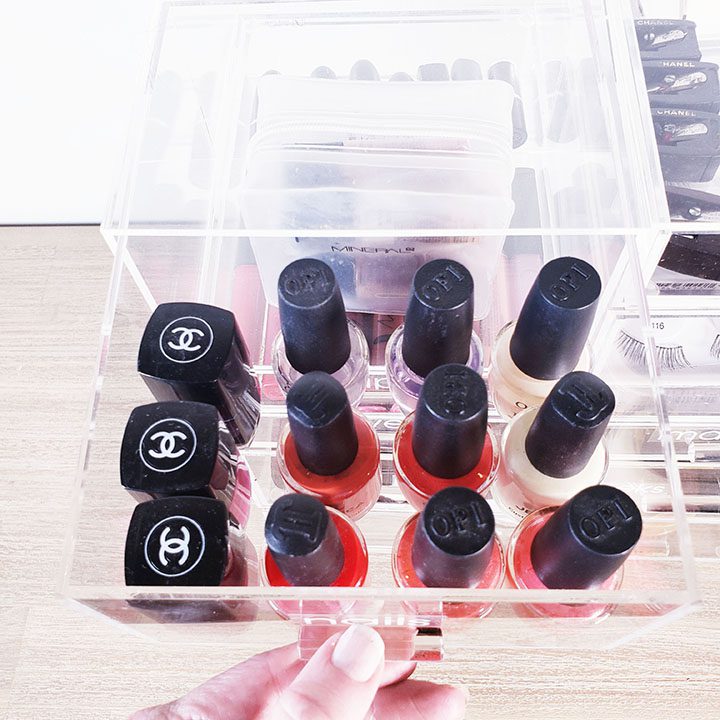 A person holding a clear box full of nail polishes, helping you organize your makeup collection.