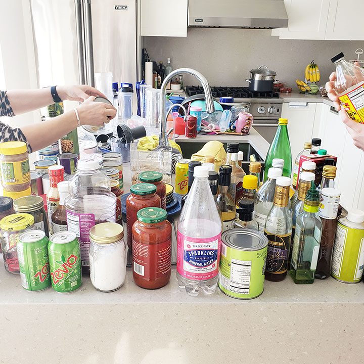 A woman is standing in front of a kitchen full of jars and bottles.