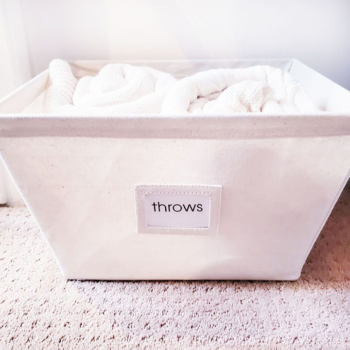 A white basket with a label that says throws, perfect for organizing your linen closet.