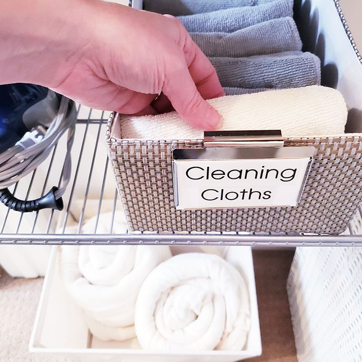 In a laundry room, an individual carefully arranges a basket filled with cleaning cloths, demonstrating how to efficiently organize your linen closet.