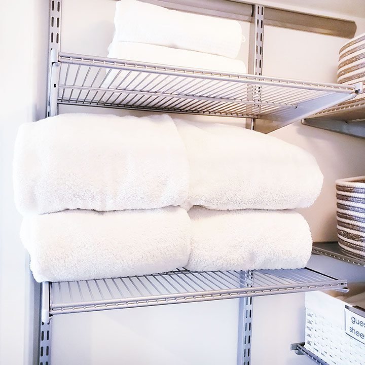 White towels are neatly organized on a shelf in a laundry room, ready to organize your linen closet.
