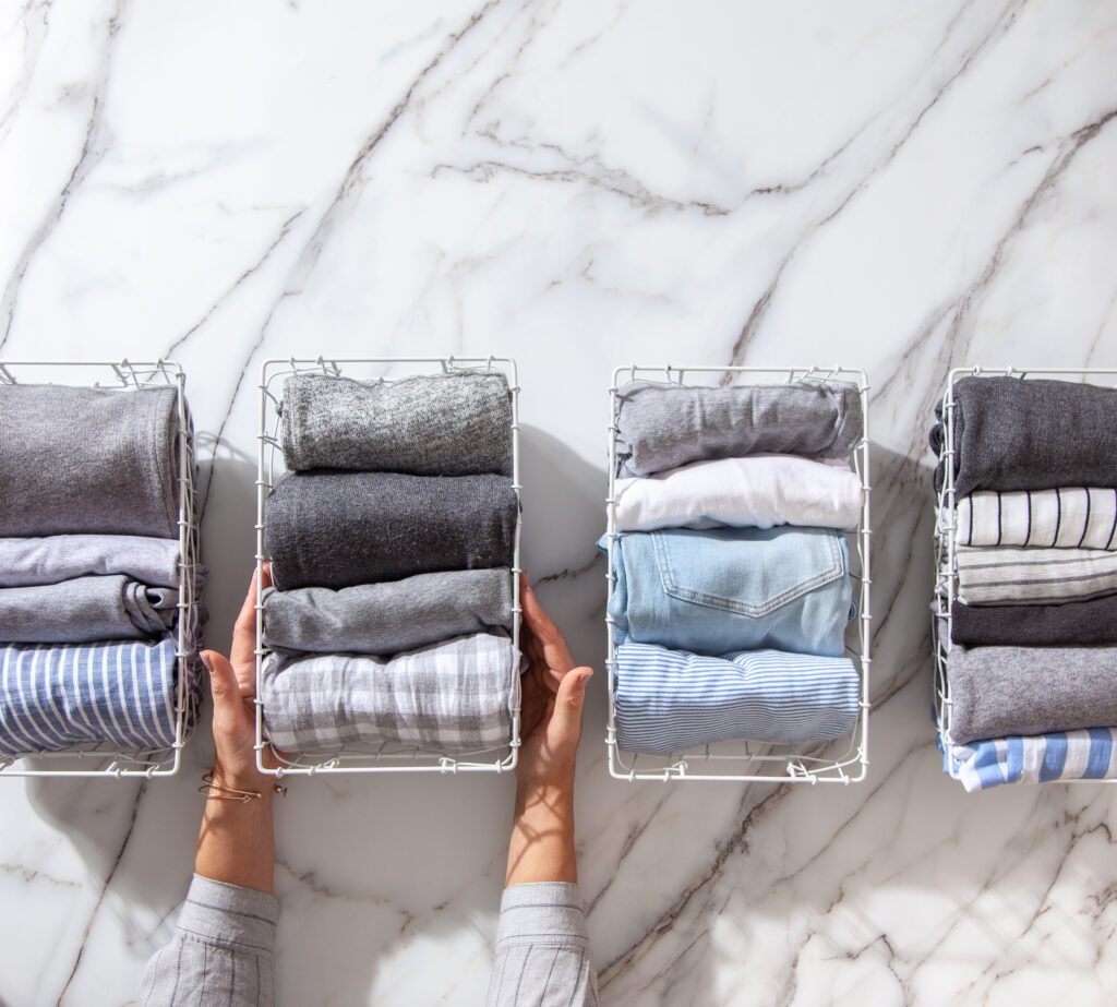 A person engaged in spring cleaning, holding a stack of clothes on a marble countertop.
