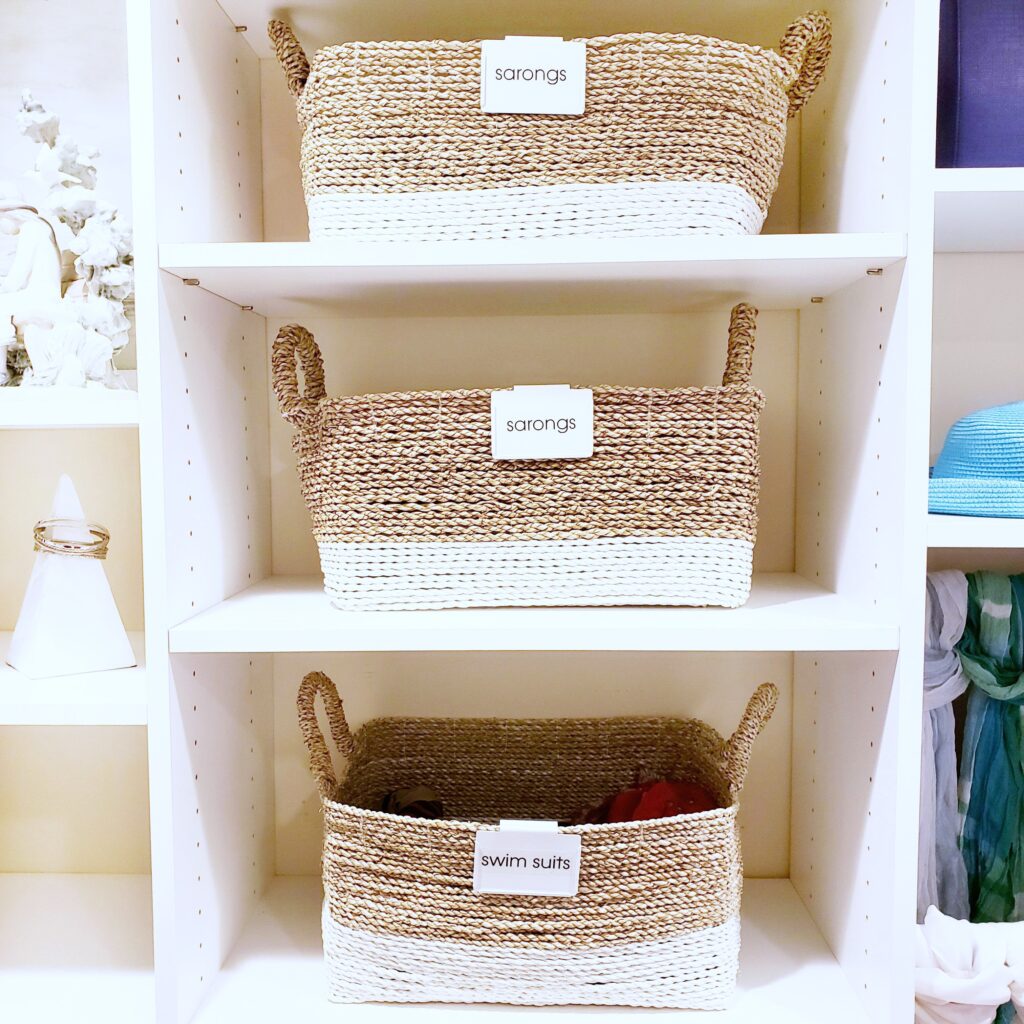 Three summer wicker baskets with labels on them in a closet.