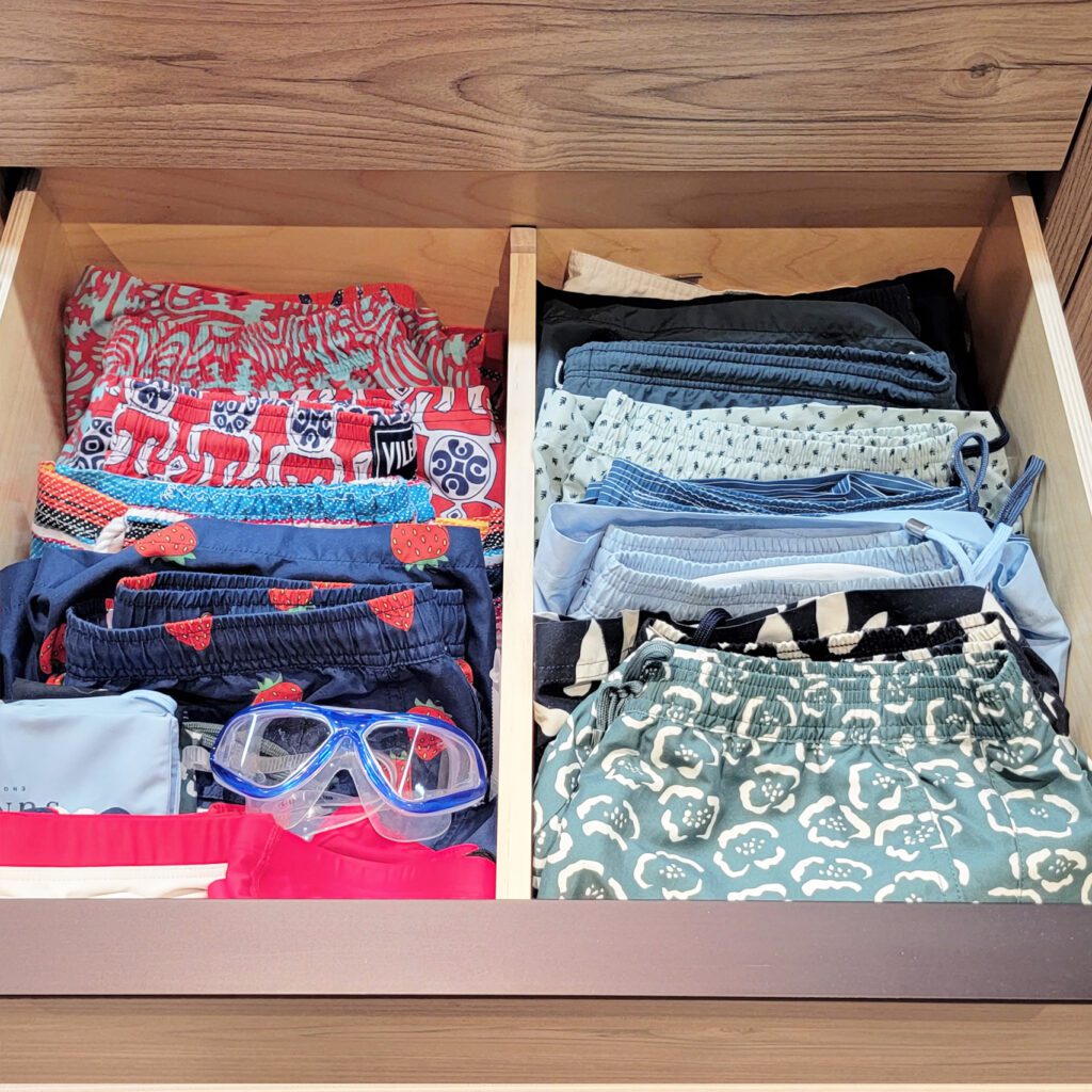 A drawer full of summer clothes and a pair of goggles.