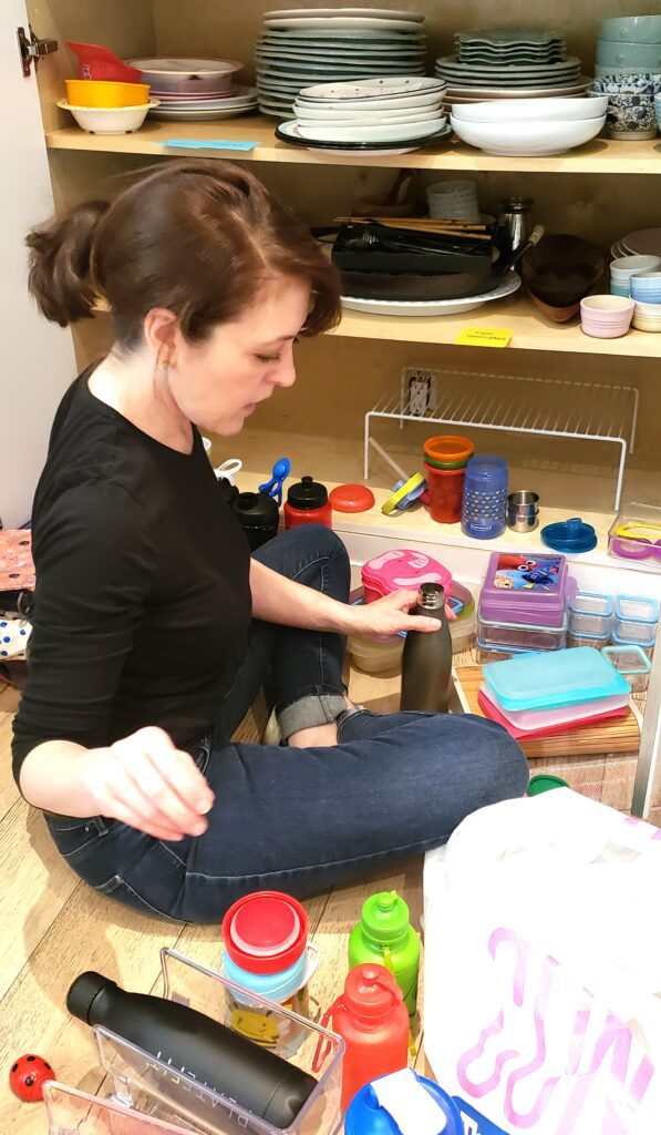 A woman sitting on the floor of a kitchen decluttering.