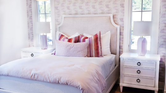 A bedroom, fresh from spring cleaning, with a white bed and pink wallpaper.