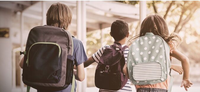 Children walking with backpacks outdoors.
